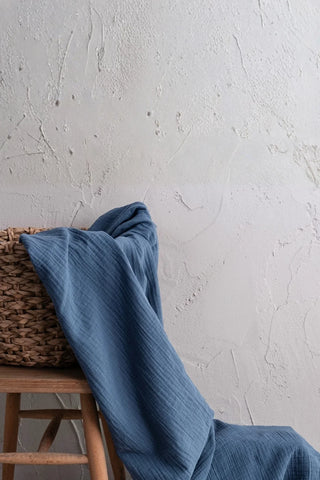 Blue muslin draped over wicker basket and stool. Handwoven 2-layer muslin cotton curtain, Denizli, OEKO-TEX. Vivamaison.