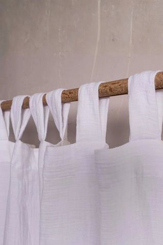 White tab loops closeup on rustic branch rod. Handwoven 2-layer muslin cotton curtain, Denizli, OEKO-TEX. Vivamaison.