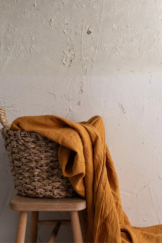 Mustard muslin draped from basket on stool. Handwoven 2-layer muslin cotton curtain, Denizli, OEKO-TEX. Vivamaison.