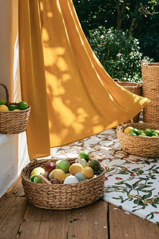 Mustard panel blowing over fruit baskets terrace. Handwoven 2-layer muslin cotton curtain, Denizli, OEKO-TEX. Vivamaison.