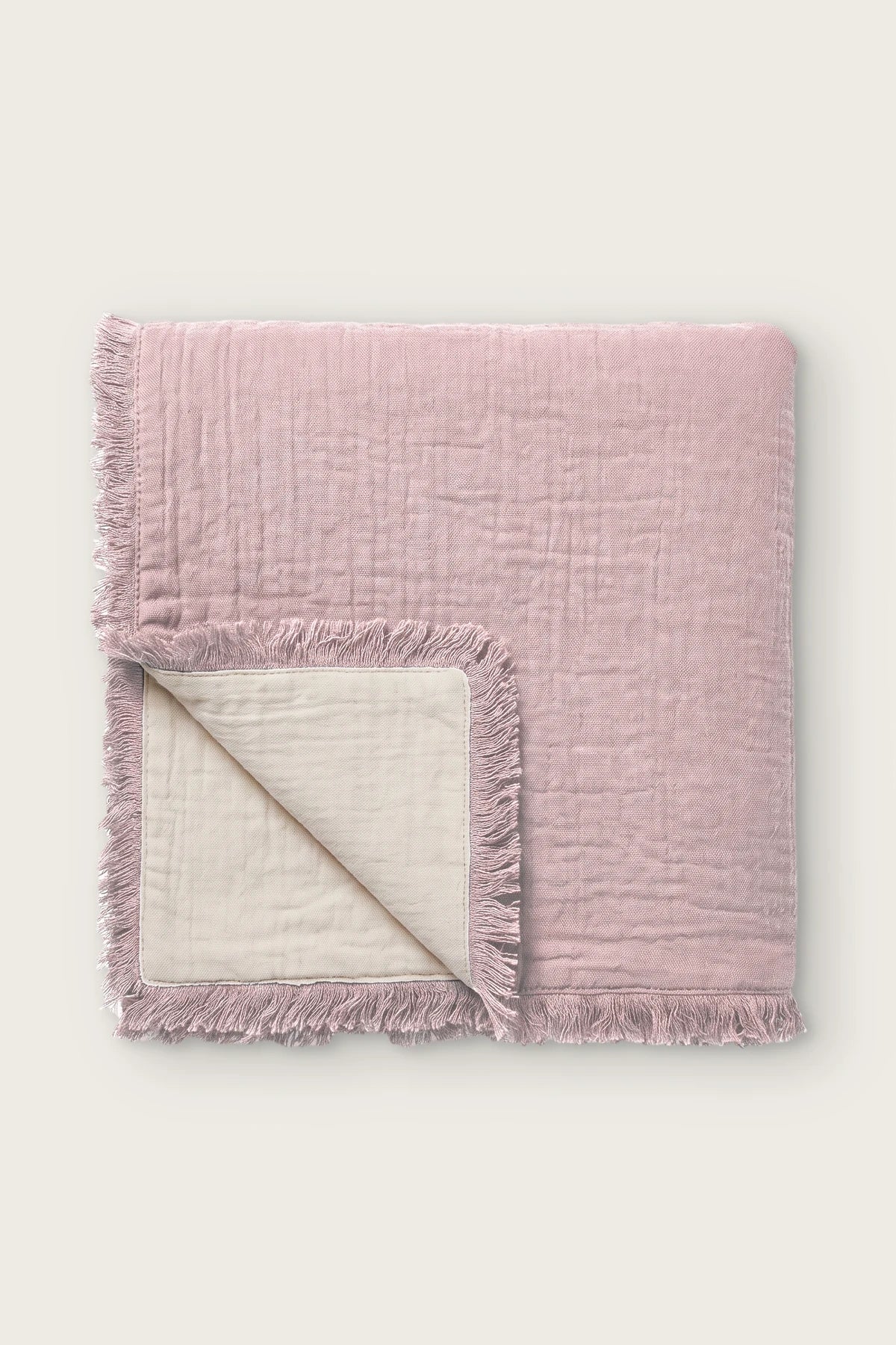 Handwoven 4-layer soft muslin fringed bedspread in pink, folded front view showing reversible cream side