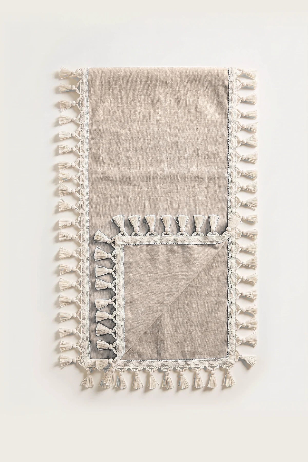 Handwoven Turkish cotton tassel table runner in brown, folded in half with corner turned back showing the tassel trim