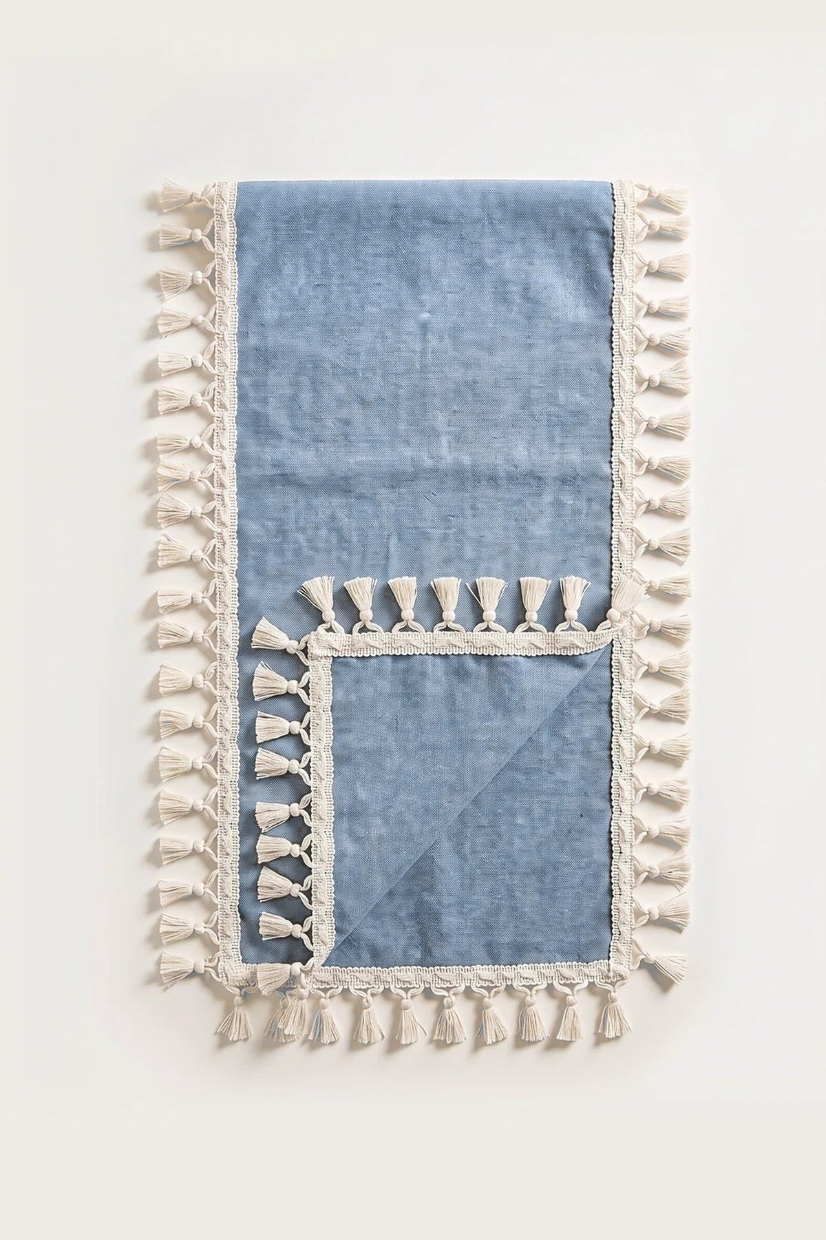 Handwoven Turkish cotton tassel table runner in navy blue, folded in half with corner turned back showing the tassel trim