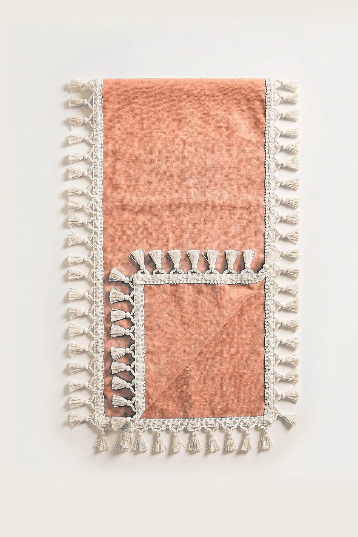 Handwoven Turkish cotton tassel table runner in orange, folded in half with corner turned back showing the tassel trim