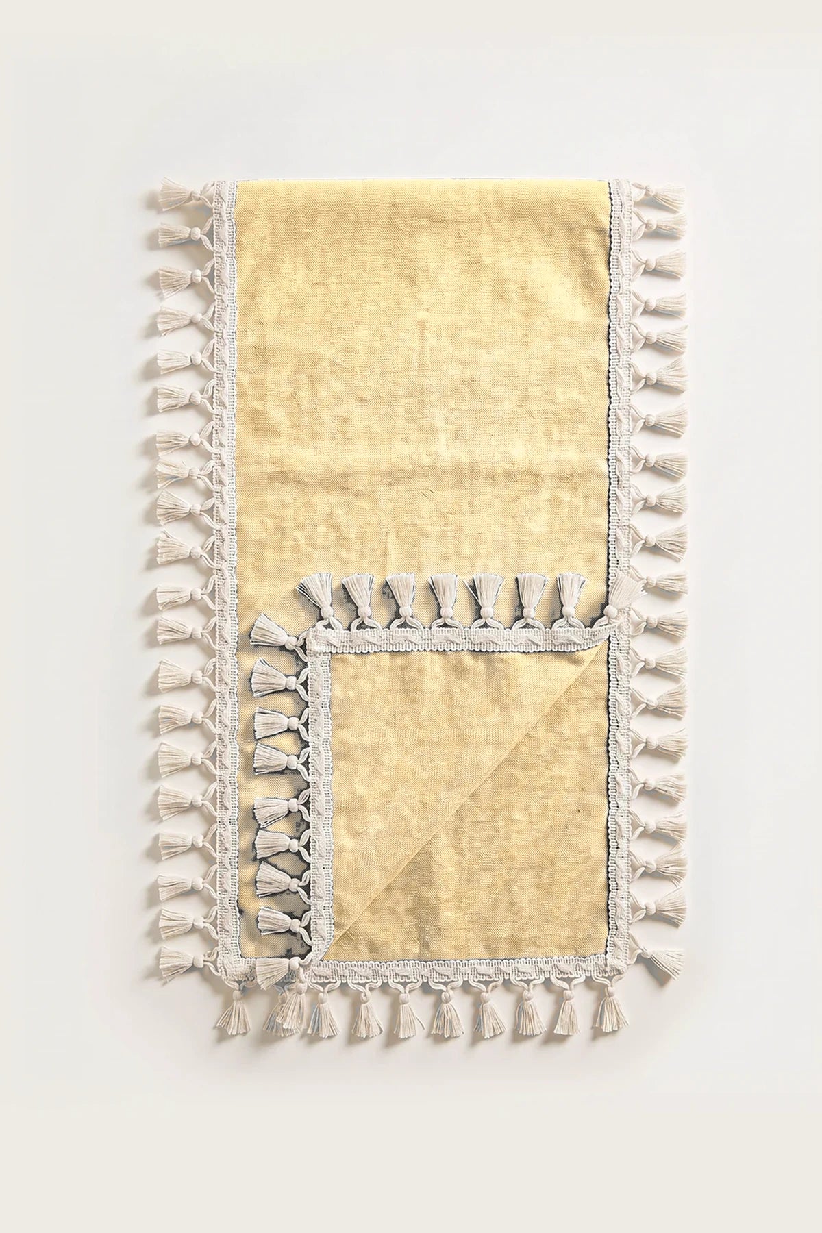 Handwoven Turkish cotton tassel table runner in yellow, folded in half with corner turned back showing the tassel trim