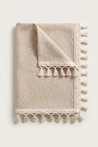 Handwoven Turkish cotton tassel tablecloth in beige, folded with corner turned back showing the tassel trim