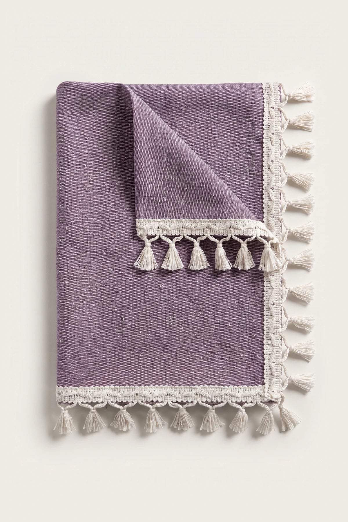 Handwoven Turkish cotton tassel tablecloth in plum, folded with corner turned back showing the tassel trim