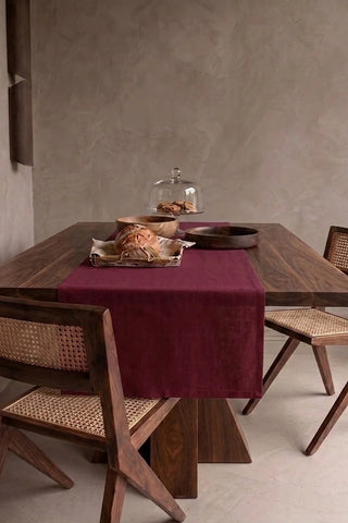 Burgundy plain linen cotton blend table runner draped over a walnut dining table with a bread basket and wooden bowls. 16 x 51 in, handmade in Denizli, OEKO-TEX. VivaMaison.