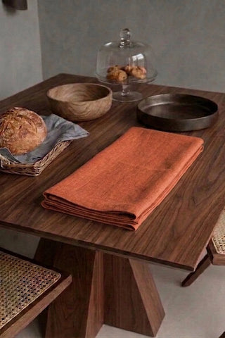 Cinnamon plain linen cotton blend table runner folded on a walnut dining table beside a bread basket. 16 x 51 in, handmade in Denizli, OEKO-TEX. VivaMaison.