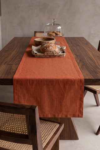 Cinnamon plain linen cotton blend table runner draped over a walnut dining table with a bread basket and wooden bowls. 16 x 51 in, handmade in Denizli, OEKO-TEX. VivaMaison.