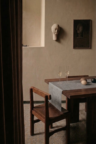 Gray plain linen cotton blend table runner on a dining table with champagne flutes, seen through a doorway. 16 x 51 in, handmade in Denizli, OEKO-TEX. VivaMaison.