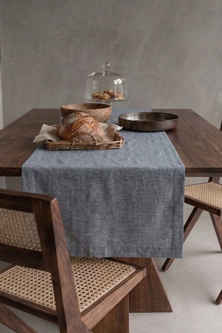 Gray plain linen cotton blend table runner draped over a walnut dining table with a bread basket and wooden bowls. 16 x 51 in, handmade in Denizli, OEKO-TEX. VivaMaison.