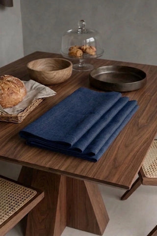 Navy plain linen cotton blend table runner folded on a walnut dining table beside a bread basket. 16 x 51 in, handmade in Denizli, OEKO-TEX. VivaMaison.
