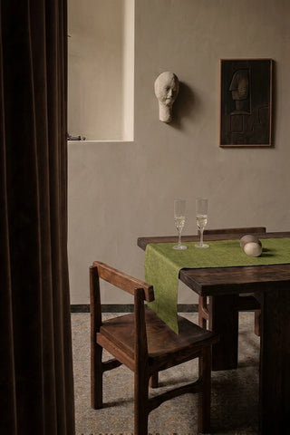 Olive Green plain linen cotton blend table runner on a dining table with champagne flutes, seen through a doorway. 16 x 51 in, handmade in Denizli, OEKO-TEX. VivaMaison.