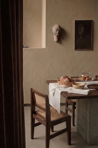 White plain linen cotton blend table runner on a dining table with a bread basket, seen through a doorway. 16 x 51 in, handmade in Denizli, OEKO-TEX. VivaMaison.