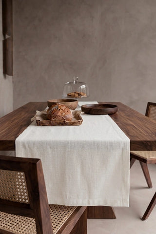 White plain linen cotton blend table runner draped over a walnut dining table with a bread basket and wooden bowls. 16 x 51 in, handmade in Denizli, OEKO-TEX. VivaMaison.