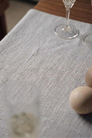 White plain linen cotton blend table runner fabric texture close-up with a wine glass and wooden spheres. 16 x 51 in, handmade in Denizli, OEKO-TEX. VivaMaison.