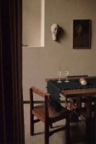 Black ruffled linen cotton blend table runner on a dining table with champagne flutes, seen through a doorway. 16 x 51 in, handmade in Denizli, OEKO-TEX. VivaMaison.