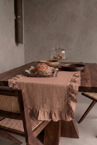 Brown ruffled linen cotton blend table runner draped over a walnut dining table with a bread basket and wooden bowls. 16 x 51 in, handmade in Denizli, OEKO-TEX. VivaMaison.