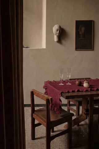 Burgundy ruffled linen cotton blend table runner on a dining table with champagne flutes, seen through a doorway. 16 x 51 in, handmade in Denizli, OEKO-TEX. VivaMaison.