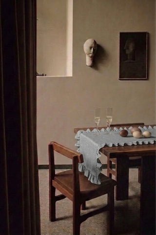Gray ruffled linen cotton blend table runner on a dining table with champagne flutes, seen through a doorway. 16 x 51 in, handmade in Denizli, OEKO-TEX. VivaMaison.