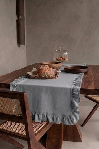 Gray ruffled linen cotton blend table runner draped over a walnut dining table with a bread basket and wooden bowls. 16 x 51 in, handmade in Denizli, OEKO-TEX. VivaMaison.