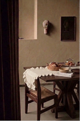 Natural ruffled linen cotton blend table runner on a dining table with a bread basket, seen through a doorway. 16 x 51 in, handmade in Denizli, OEKO-TEX. VivaMaison.