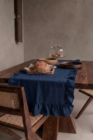 Navy ruffled linen cotton blend table runner draped over a walnut dining table with a bread basket and wooden bowls. 16 x 51 in, handmade in Denizli, OEKO-TEX. VivaMaison.