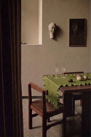 Olive Green ruffled linen cotton blend table runner on a dining table with champagne flutes, seen through a doorway. 16 x 51 in, handmade in Denizli, OEKO-TEX. VivaMaison.