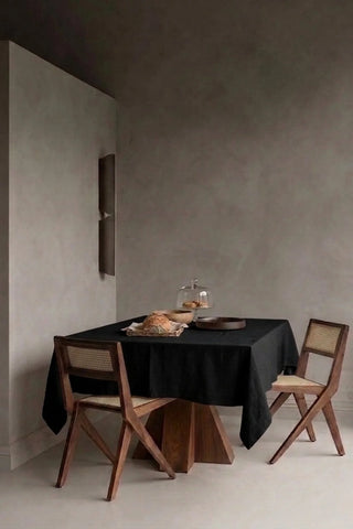 Black plain linen cotton blend tablecloth on a dining table in a modern dining room with cane chairs. 9 sizes, handmade in Denizli, OEKO-TEX. VivaMaison.