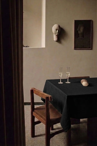 Black plain linen cotton blend tablecloth on a dining table with champagne flutes, seen through a doorway. 9 sizes, handmade in Denizli, OEKO-TEX. VivaMaison.