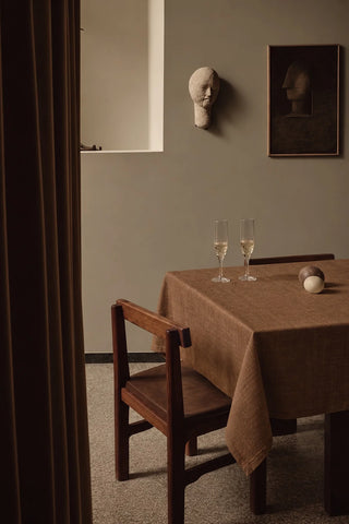 Brown plain linen cotton blend tablecloth on a dining table with champagne flutes, seen through a doorway. 9 sizes, handmade in Denizli, OEKO-TEX. VivaMaison.