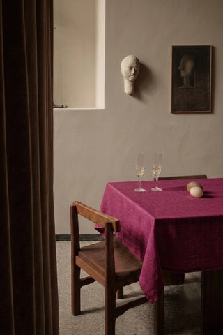 Burgundy plain linen cotton blend tablecloth on a dining table with champagne flutes, seen through a doorway. 9 sizes, handmade in Denizli, OEKO-TEX. VivaMaison.