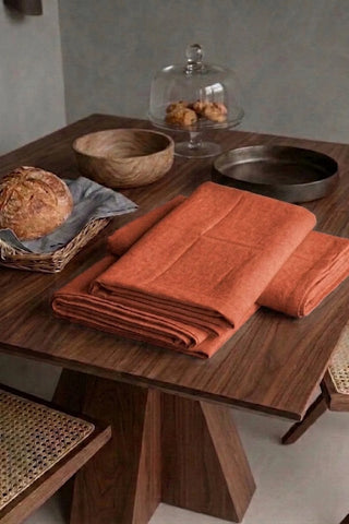 Cinnamon plain linen cotton blend tablecloth folded on a walnut dining table beside a bread basket. 9 sizes, handmade in Denizli, OEKO-TEX. VivaMaison.