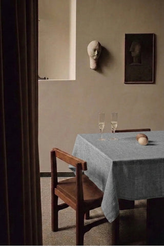 Gray plain linen cotton blend tablecloth on a dining table with champagne flutes, seen through a doorway. 9 sizes, handmade in Denizli, OEKO-TEX. VivaMaison.