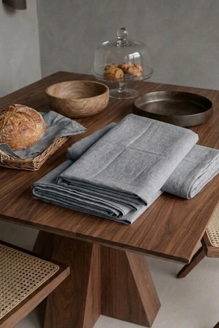 Gray plain linen cotton blend tablecloth folded on a walnut dining table beside a bread basket. 9 sizes, handmade in Denizli, OEKO-TEX. VivaMaison.