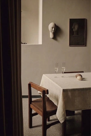 Natural plain linen cotton blend tablecloth on a dining table with champagne flutes, seen through a doorway. 9 sizes, handmade in Denizli, OEKO-TEX. VivaMaison.
