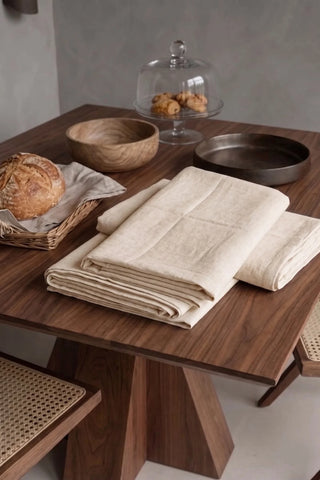Natural plain linen cotton blend tablecloth folded on a walnut dining table beside a bread basket. 9 sizes, handmade in Denizli, OEKO-TEX. VivaMaison.