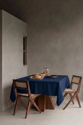 Navy plain linen cotton blend tablecloth on a dining table in a modern dining room with cane chairs. 9 sizes, handmade in Denizli, OEKO-TEX. VivaMaison.
