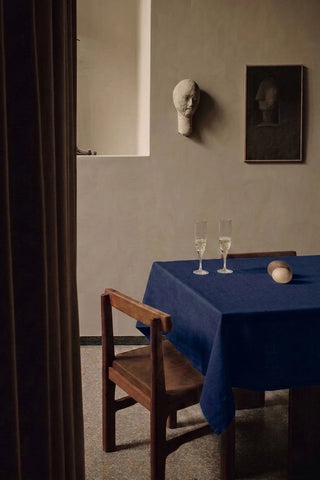 Navy plain linen cotton blend tablecloth on a dining table with champagne flutes, seen through a doorway. 9 sizes, handmade in Denizli, OEKO-TEX. VivaMaison.