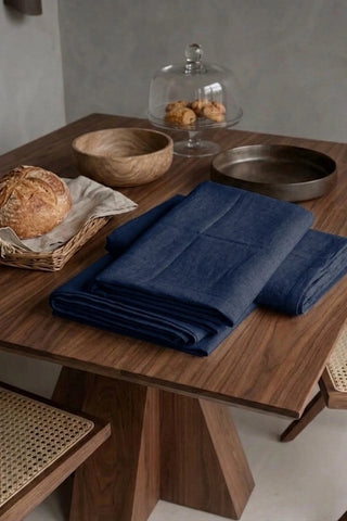 Navy plain linen cotton blend tablecloth folded on a walnut dining table beside a bread basket. 9 sizes, handmade in Denizli, OEKO-TEX. VivaMaison.