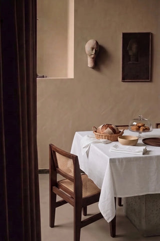 White plain linen cotton blend tablecloth on a dining table with a bread basket, seen through a doorway. 9 sizes, handmade in Denizli, OEKO-TEX. VivaMaison.