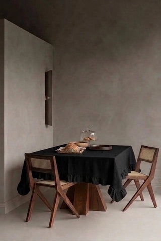 Black ruffled linen cotton blend tablecloth on a dining table in a modern dining room with cane chairs. 9 sizes, handmade in Denizli, OEKO-TEX. VivaMaison.