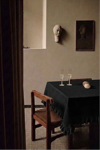 Black ruffled linen cotton blend tablecloth on a dining table with champagne flutes, seen through a doorway. 9 sizes, handmade in Denizli, OEKO-TEX. VivaMaison.