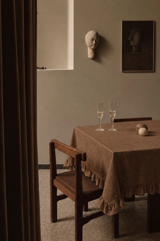 Brown ruffled linen cotton blend tablecloth on a dining table with champagne flutes, seen through a doorway. 9 sizes, handmade in Denizli, OEKO-TEX. VivaMaison.