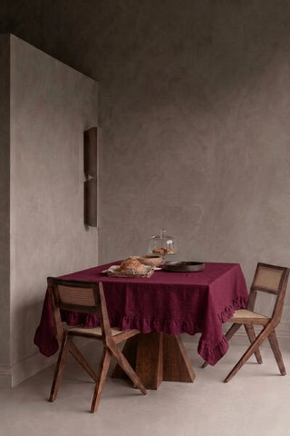 Burgundy ruffled linen cotton blend tablecloth on a dining table in a modern dining room with cane chairs. 9 sizes, handmade in Denizli, OEKO-TEX. VivaMaison.