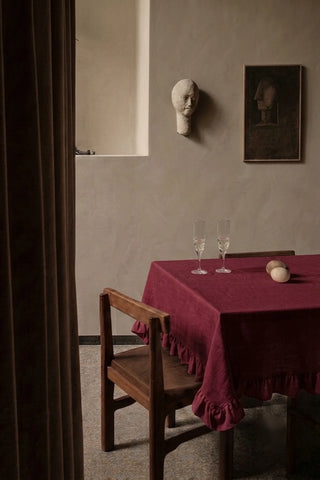 Burgundy ruffled linen cotton blend tablecloth on a dining table with champagne flutes, seen through a doorway. 9 sizes, handmade in Denizli, OEKO-TEX. VivaMaison.
