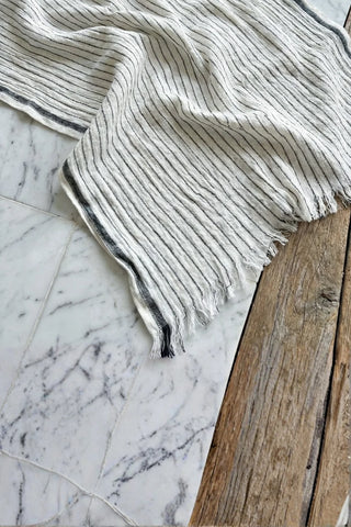 Hand-twisted fringe detail of muslin striped turkish cotton beach towel peshtemal with black stripes on marble - VivaMaison