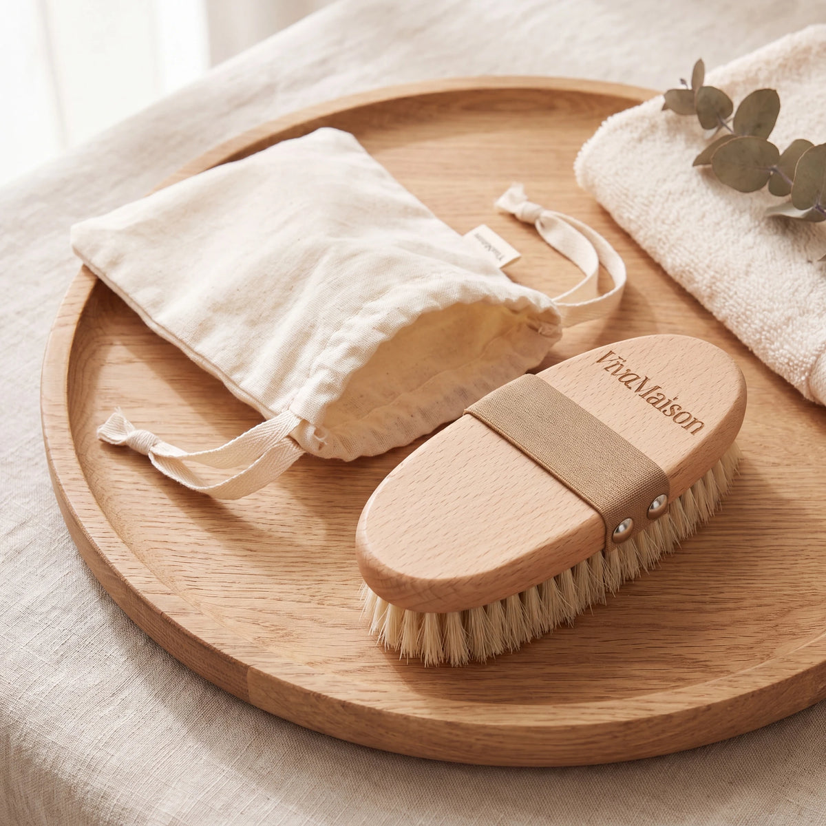 Natural bristle dry body brush with its cotton drawstring pouch on a wooden tray - VivaMaison