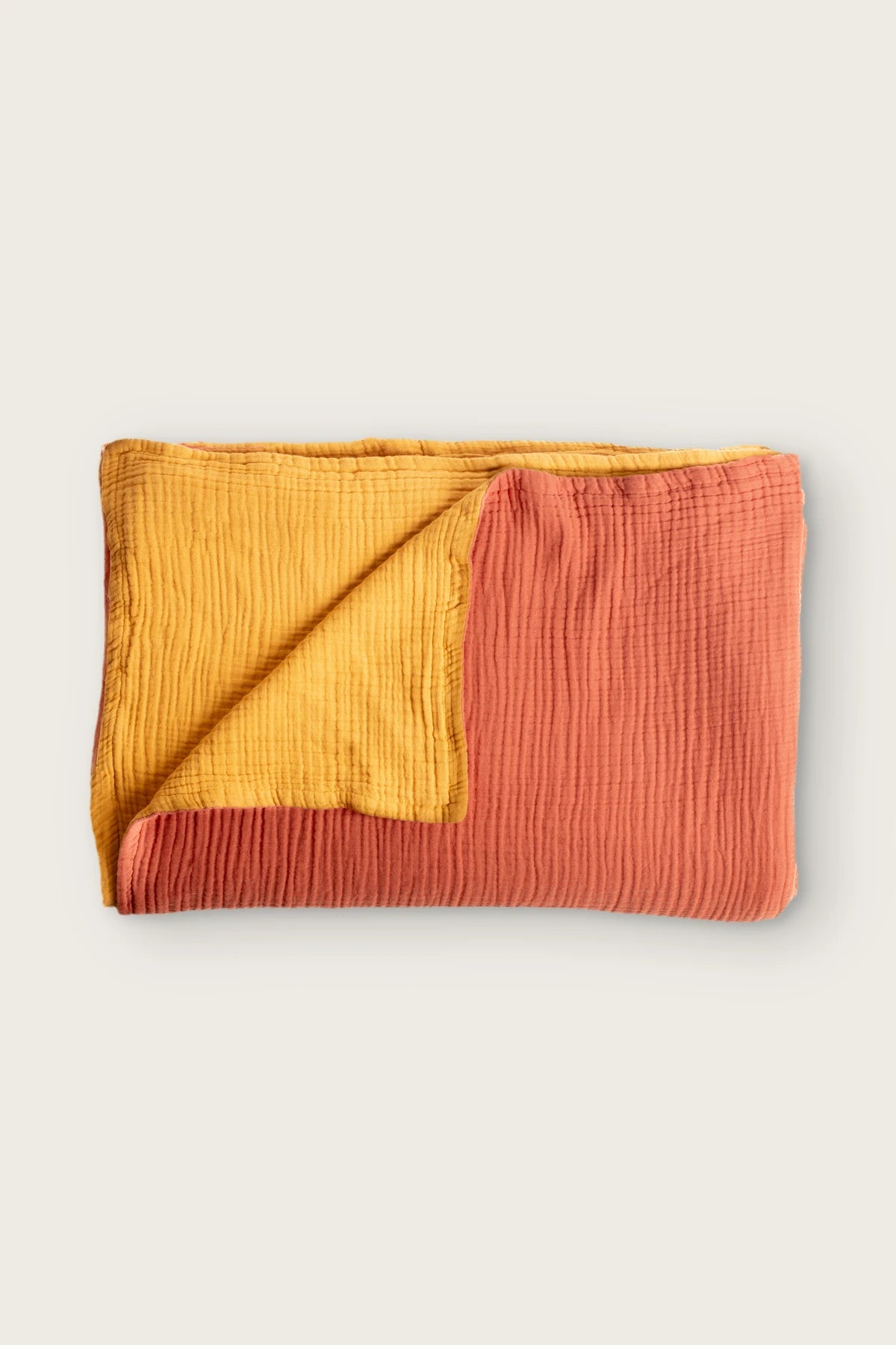 Reversible 8-layer muslin bedspread in coral / mustard, folded flat lay showing both sides